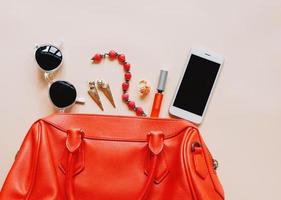 Flat lay of red leather woman bag open out with cosmetics, accessories and smartphone on yellow background photo