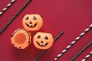 Flat lay style of halloween party concept with decorative pumpkins and black fancy straw on red background, copy space photo