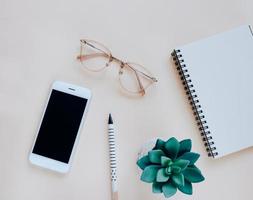 Flat lay of workspace desk with smartphone, notebook, eyeglasses, pen and plant, minimal style photo