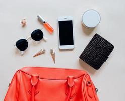 Flat lay of red leather woman bag open out with cosmetics, accessories and smartphone on yellow background photo