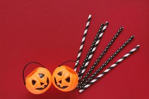 Flat lay style of halloween party concept with decorative pumpkins and black fancy straw on red background, copy space photo