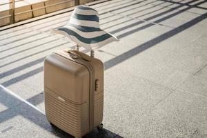 una maleta con sombrero de verano en la sala de embarque del aeropuerto, concepto de viajes y vacaciones foto