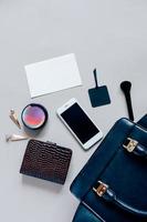 Flat lay of black leather woman bag open out with cosmetics, accessories and smartphone and blank card of paper on grey background with copy space photo