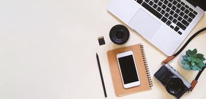 Desktop flat lay photo of workspace desk with laptop, camera, tablet, smartphone, lens and notebook on yellow modern background, top view and copy space, mood board style and banner panoramic style