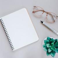 Flat lay of minimal workspace desk with notebook, eyeglasses and green plant, copy space photo