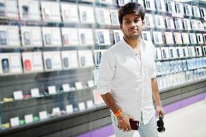 Indian man customer buyer at mobile phone store with wireless earphones connect to his smartphone. South asian peoples and technologies concept. Cellphone shop. photo