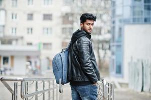 Stylish and casual asian man in black leather jacket with backpack posed at street. photo