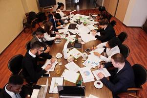 Multiracial business team addressing meeting around boardroom table, working together and write something on papers. photo