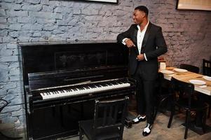 Strong powerful african american man in black suit standing against piano. photo