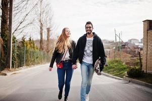 Cool multiracial couple walking together with longboard. photo