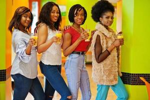 cuatro jóvenes africanas con jugos de naranja posan en un restaurante de comida rápida de colores brillantes. foto