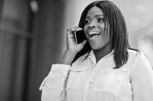 Formally dressed african american business woman in white blouse and red trousers with mobile phone. Successful dark skinned businesswoman. photo