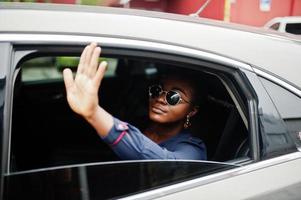 una rica mujer africana de negocios con gafas de sol se sienta en un auto todoterreno y muestra la mano desde la ventana. foto