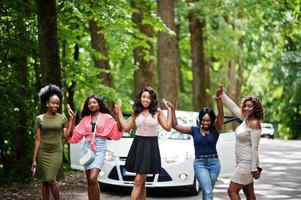 grupo de cinco afroamericanos felices caminando contra un auto blanco. foto