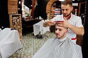 un joven barbudo que se corta el pelo con un peluquero mientras se sienta en una silla en la barbería. alma de barbero. foto