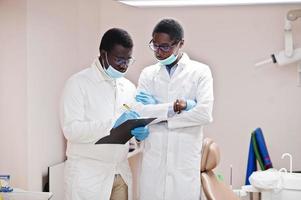dos colegas médicos afroamericanos trabajando juntos, discutiendo y mirando el portapapeles en la clínica. foto