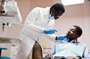 African american man patient in dental chair. Dentist office and doctor practice concept. Professional dentist helping his patient at dentistry medical. Drilling patient's teeth in clinic. photo