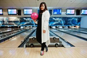 Stylish asian woman standing at bowling alley with ball at hand. photo