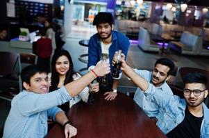 Group of stylish asian friends wear on jeans sitting at table and cheering with soda bottles in club. photo