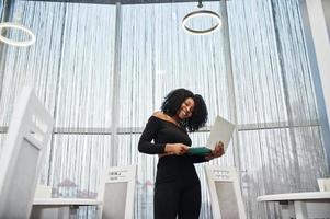 Fashionable young beautiful african american business woman with afro hairstyle wear in elegant black, stand with laptop at hands. photo