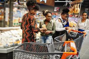 Group of five african womans with shopping carts choose cheese in supermarket. photo