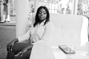 mujer de negocios afroamericana vestida formalmente con blusa blanca y pantalón rojo sentada en la terraza al aire libre. exitosa empresaria de piel oscura. foto