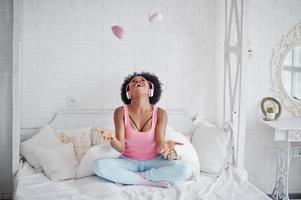 Young african american woman sitting in bed and listen music on earphones. photo