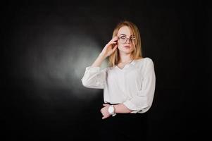 retrato de estudio de mujer de negocios rubia con gafas, blusa blanca y falda negra sobre fondo oscuro. concepto de mujer exitosa y chica elegante. foto