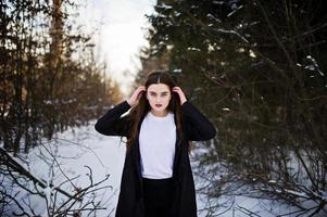 Fashionable long legs brunette model in long black cloak posed outdoor at winter day. photo