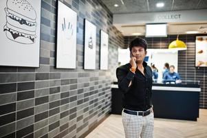 hombre indio hablando por teléfono móvil mientras espera su pedido en el café de comida rápida. foto