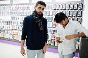dos indios sirven al comprador del cliente en la tienda de teléfonos móviles con sus nuevos teléfonos inteligentes. concepto de pueblos y tecnologías del sur de Asia. tienda de celulares foto