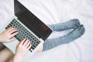 Top view of woman legs in socks and using laptop on cozy bed, lifestyle concept photo