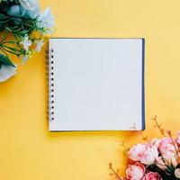 Flat lay of minimal workspace blank notebook with flower on yellow background, spring and summer concept photo