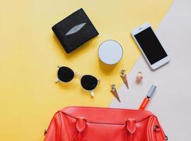 Flat lay of red leather woman bag open out with cosmetics, accessories, wallet and smartphone on yellow background photo