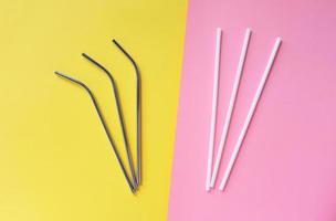 Flat lay of reusable stainless steel straw with plastic straw on bright pink and yellow color background, sustainable lifestyle and zero waste concept photo