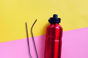 Flat lay of metallic stainless straws and reusable bottle for drink on bright pink and yellow background, sustainable product lifestyle and zero waste concept, copy space photo