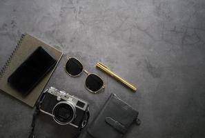 Flat lay of workspace desk of male gadget and accessories, smartphone, sunglasses, wallet, camera and notebook on dark stone background, top view with copy space, business and lifestyle concept photo