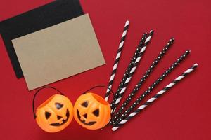 Flat lay style of halloween party concept with decorative pumpkins and black fancy straw with blank card on red background photo
