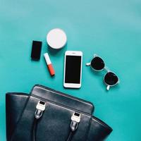 Flat lay of black leather woman bag open out with cosmetics, accessories and smartphone on green background photo