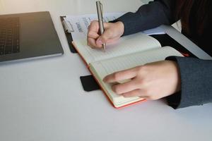 mujer sosteniendo está escribiendo en un cuaderno con un bolígrafo en la oficina. foto