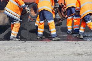 un trabajador de la carretera está esparciendo asfalto fresco con palas sobre el área de reparación para reparar una sección de la carretera. foto