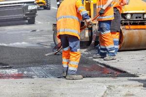 un grupo de trabajadores de la carretera con monos naranjas está reparando una sección de la calzada enrollando asfalto fresco. foto