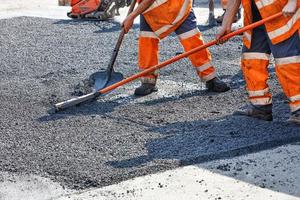 un equipo de trabajo de constructores de carreteras nivela manualmente el asfalto caliente con palas y niveles de metal. foto