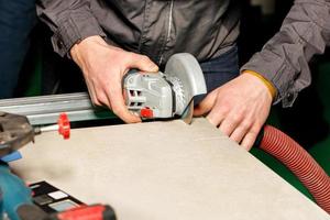 A worker cuts a ceramic-metal plate with a hand-held electric grinder with a diamond disc and dust extraction. photo