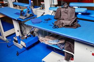 Professional work tables with blue upholstery fabric of a dress cutter in an atelier studio with a steam iron and various fabrics. photo