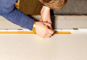 A worker marks out a sheet of drywall with a pencil and a wooden folding rule. Close-up of a worker's hands. photo