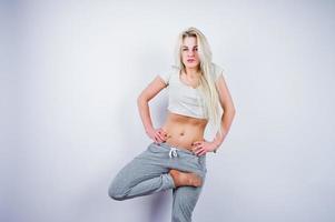 Blonde sporty girl makes stretching at studio against white background. photo