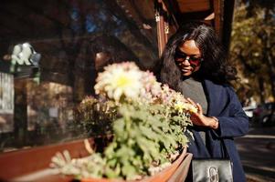 elegante chica afroamericana con abrigo azul y gafas de sol posadas en el soleado día de otoño. mujer modelo africana. foto