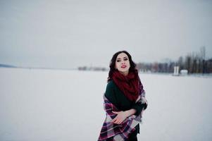 Brunette girl in green sweater and red scarf with plaid outdoor frozen lake on evening winter day. photo