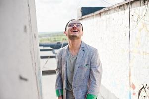 hombre macho con estilo soñador en traje gris, sombrero y gafas posadas en el techo. foto